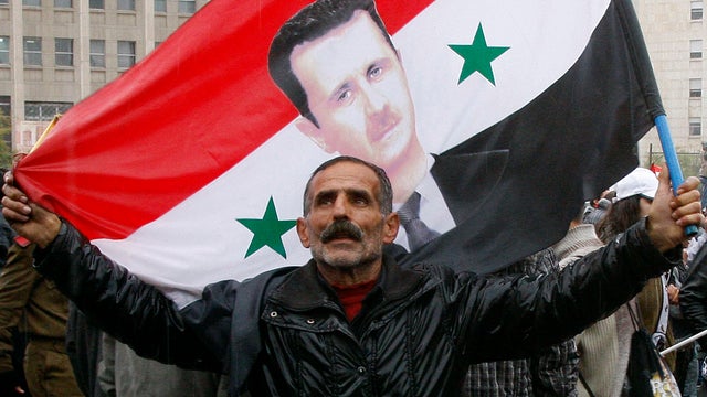 A pro-Syrian regime protester holds up a Syrian flag bearing a portrait of Syrian President Bashar Assad in Damascus, Syria, Nov. 16, 2011. 