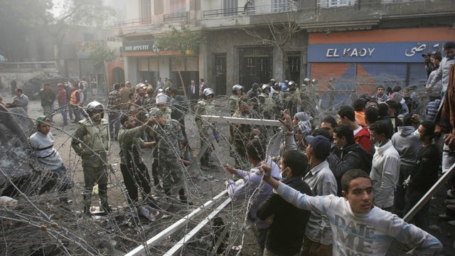 Egyptian protesters stand behind a barbed wire barricade in Tahrir Square 
