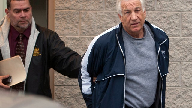 Former Penn State assistant football coach Jerry Sandusky, right, leaves the office of Centre County District Justice Daniel A. Hoffman under escort by Pennsylvania State Police and Attorney General's Office officials in Bellefonte, Pa., on Thursday, Dec. 