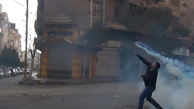 A protester in the flahspoint central Syrian city of Homs throws a tear gas bomb back towards security forces, on December 27, 2011.  