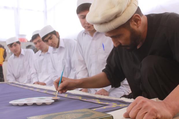 Calligrapher Mohammed Sabeer Hussani's apprentices watch as he carefully works on the edges of a page 