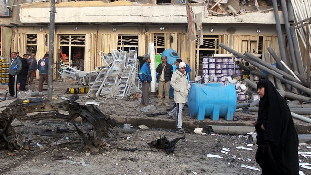 An Iraqi woman walks past civilians inspecting damages at the site of a blast after a bomb ripped through a group of workers in Sadr City in Baghdad Jan. 24, 2012. A series of car bombs exploded in Shiite areas of Baghdad, killing at least nine people and 