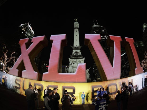 football fans pose for photos in front of the Super Bowl XLVI logo on Monument Circle 