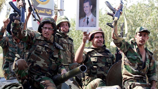 Syrian soldiers raise their weapons to a government-guided media tour while holding a picture of Syrian President Bashar al-Assad as they leave the eastern city of Deir Zor Aug. 16, 2011. 