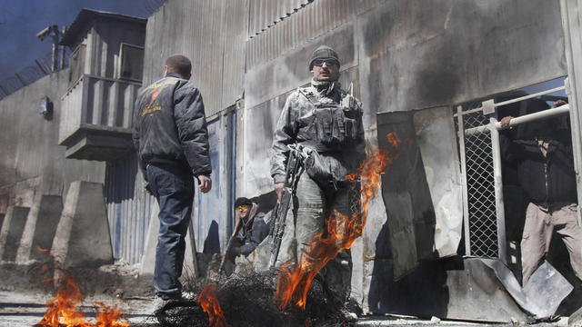 Security guards stand as black smoke rises from tires which were burnt by protesters 