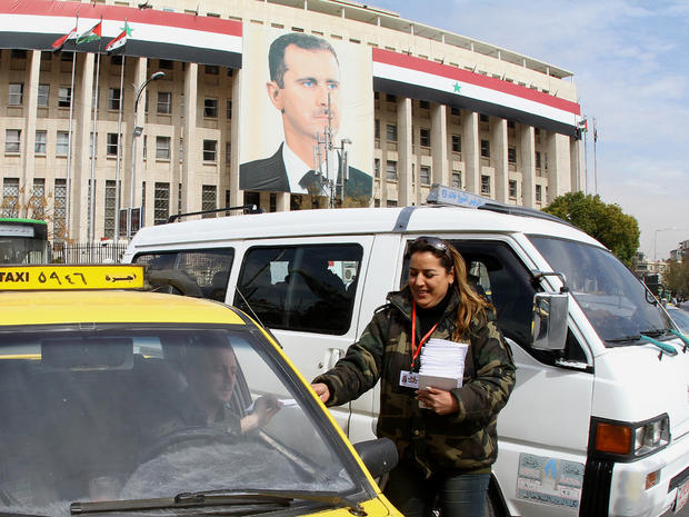 A woman hands a copy of the draft constitution to a taxi driver in Damascus 