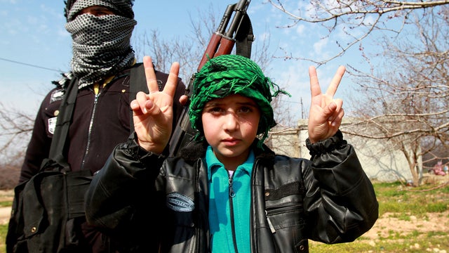 A child flashes the V-sign for victory as a rebel of the Free Syrian Army is seen in the Syrian village of Jussiyeh March 6, 2012, just across from Lebanon's eastern Bekaa region. 