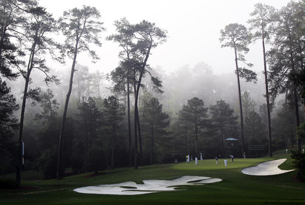 Players putt on the 10th green in the morning fog 