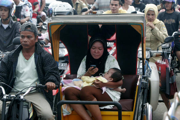 An Acehnese woman checks her mobile phone as she and her baby evacuate to higher ground 