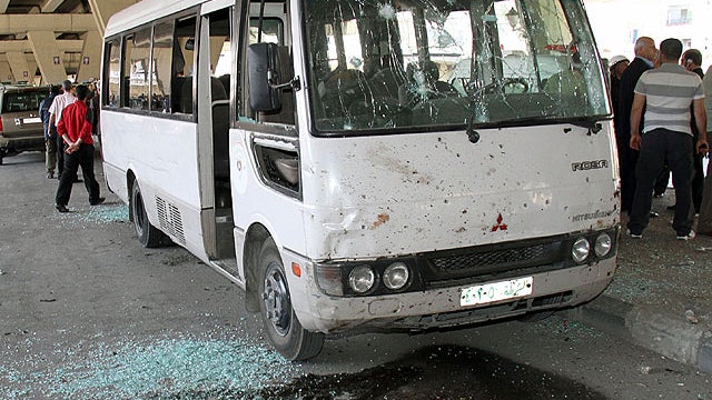 Syrian investigators, right, gather next to a damaged police bus that was attacked by an explosion in the Midan neighborhood of Damascus, Syria, on April 27, 2012.  