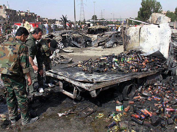 Syrian soldiers check a burned truck in front of a damaged military intelligence building where two bombs exploded, at Qazaz neighborhood in Damascus, Syria, on May 10, 2012. 