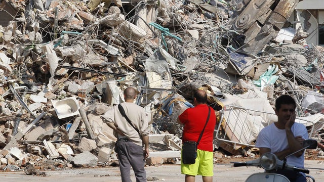 People stand in front of a collapsed building in Cavezzo, northern Italy 