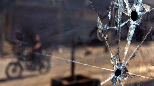 A Syrian man riding a motorcycle is seen reflected in a shop's glass door with bullet holes in the town of Taftanaz, Syria, June 5, 2012. 