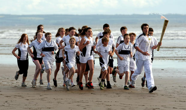 Joseph Forrest and children from Madras College run along West Sands beach with the Olympic Torch on June 13, 2012 in St Andrews, Scotland.  