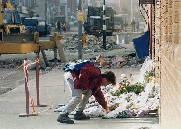 A young man lays flowers near remains of a shop in which ten people were killed 