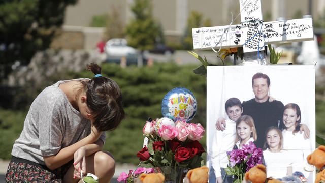 Ashley Deuell, 18, kneels next to a cross and family photo of Gordon Cowden, who was a friend of her family, Tuesday, July 24, 2012 at a growing memorial to the victims of last Friday's mass shooting in a movie theater in Aurora, Colo. 