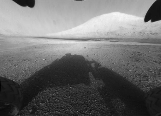 This image taken by NASA's Curiosity shows what lies ahead for the rover -- its main science target, informally called Mount Sharp Monday, Aug. 6, 2012. The rover's shadow can be seen in the foreground, and the dark bands beyond are dunes. Rising up in th 