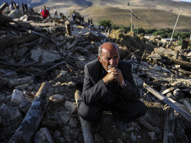 A victim of the twin earthquakes which rattled northeast Iran sits on ruins 