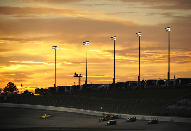 A group of cars go into turn one as the sun sets 