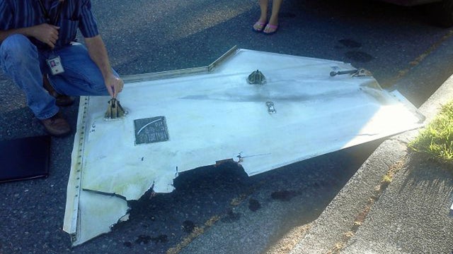 Man examines piece of metal that appears to be a landing gear door that fell from plane in Kent, Wash. Friday  
