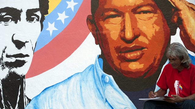 An artist draws next to a painting of Venezuelan President Hugo Chavez, right, and Latin American independence hero Simon Bolivar in Caracas, Venezuela, Jan. 3, 2013. 