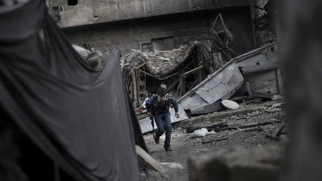 A 15-year-old rebel fighter runs across a road behind a makeshift barrier 