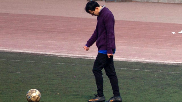 A Chinese college student kicks a soccer ball  