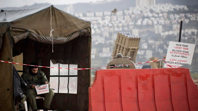 Israeli soldier reads a newspaper next to an Iron Dome short-range missile defense system 