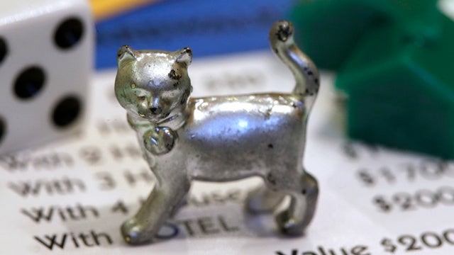 The newest Monopoly token, a cat, rests on a Boardwalk deed next to a die and houses at Hasbro Inc. headquarters, in Pawtucket, R.I., Tuesday, Feb. 5, 2013. Voting on Facebook determined that the cat would replace the iron token.  