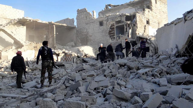 Syrian rebels stand in the rubble of damaged buildings  
