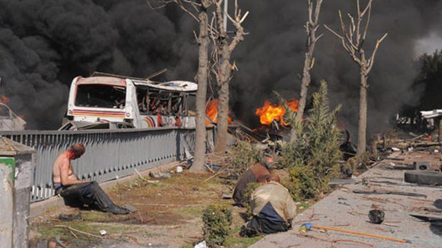 Injured people sitting near the scene of a huge explosion at a security checkpoint in central Damascus 