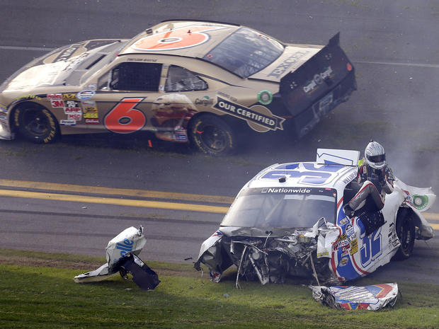 Driver Kyle Larson climbs out of his car as Trevor Bayne (6) rolls past after a crash at the conclusion of the NASCAR Nationwide Series auto race Feb. 23, 2013, at Daytona International Speedway in Daytona Beach, Fla. 