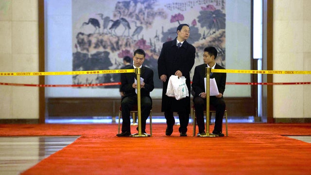 A security person eyes a man leaving with plastic bags at the Great Hall of the People during a lull in activities at the annual congress meetings in Beijing, China, Wednesday, March 6, 2013. 