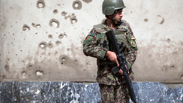 An Afghan Army soldier takes position next to a shrapnel-ridden wall at the gate of the Afghan Defense Ministry after a suicide bomber on a bicycle struck outside the ministry in Kabul, Afghanistan, March 9, 2013. 
