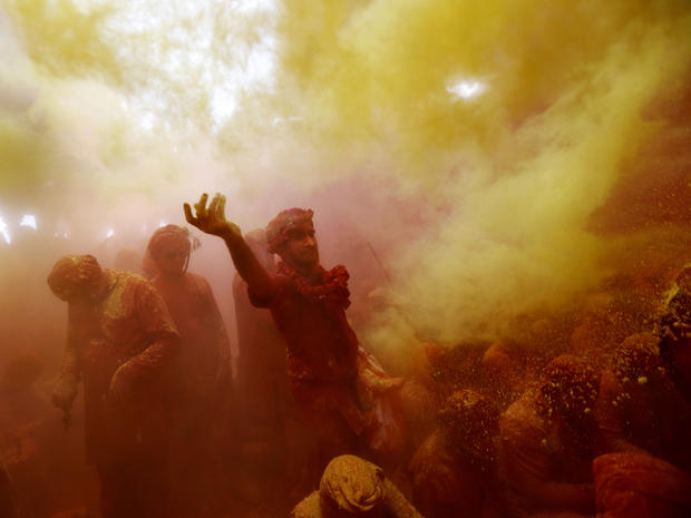 A Hindu man from the village of Nangaon, India, throws colored powder on others as they sit on the floor during prayers at the Ladali, or Radha temple, before the procession for the Lathmar Holi festival in the legendary hometown of Radha, consort of Hind 