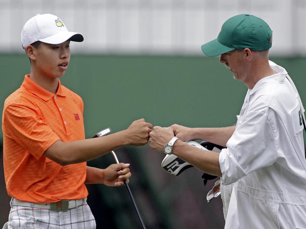 Amateur Guan Tianlang, of China, touches fists with his caddie, Brian Tam, after putting on the third hole during the second round of the Masters golf tournament April 12, 2013, in Augusta, Ga. 