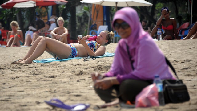 A Muslim woman wearing a veil sits in front of foreign tourists wearing bikinis on Kuta beach in Bali 