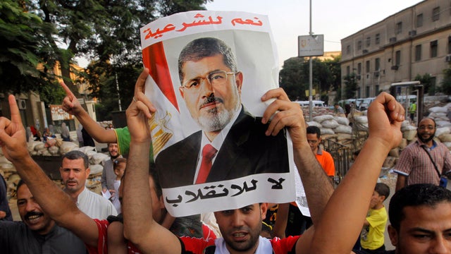 Supporters of Egypt's ousted President Mohammed Morsi walk through makeshift barriers to a sit-in at Nahda Square, which is fortified with multiple walls of bricks, tires, metal barricades and sandbags, where protesters have installed their camp near Cair 