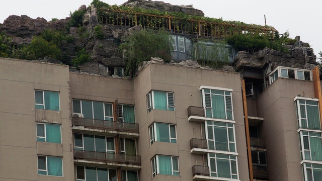 A rooftop villa complete with rocks and flora built on top of a high-rise residential building 