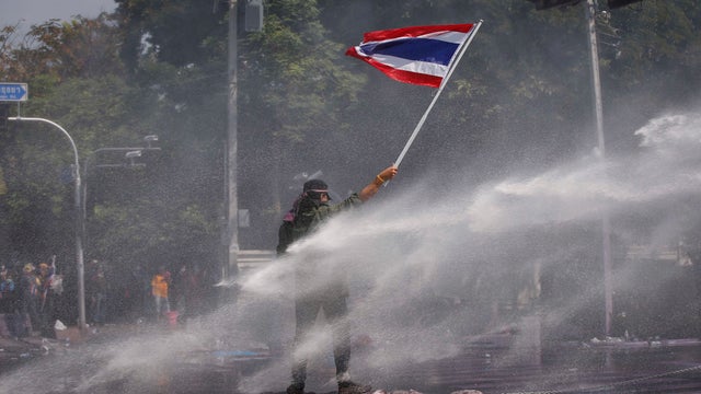 An Anti-government protester waves Thai National Flag as he is hit by water cannon fired by police during a protest rally in Bangkok 