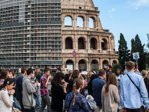 Tourists and locals walk in front of the Colosseum, partially covered in scaffolding weeks before restoration work began, Oct. 9, 2013 in Rome 