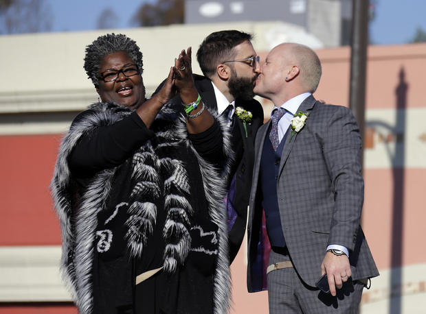 Aubrey Loots, right, and Danny Leclair, the first gay couple to be married aboard a float in the Tournament of Roses, kiss after being wed by the Rev. Alfreda Lanoix of the Unity Fellowship Church of Christ, left, aboard the AIDS Healthcare Foundation float in the 125th Rose Parade in Pasadena, Calif., Jan. 1, 2014. 