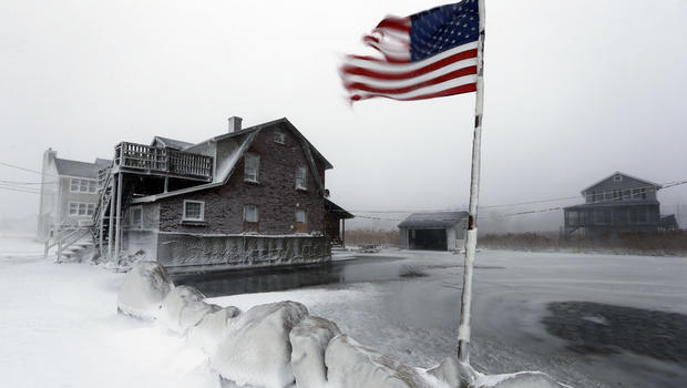 A tattered flag flies by a flooded yard along the shore in Scituate, Mass., Jan. 3, 2014. 