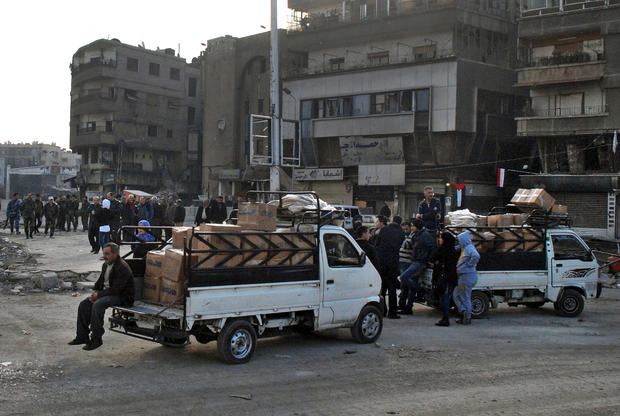 In this photo released by the Syrian official news agency SANA, trucks carry U.N. supplies at the besieged refugee camp of Yarmouk on the southern edge of the Syrian capital of Damascus 