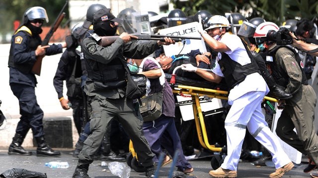 An armed Thai policeman, center, aims his rubber bullet rifle as medic team 