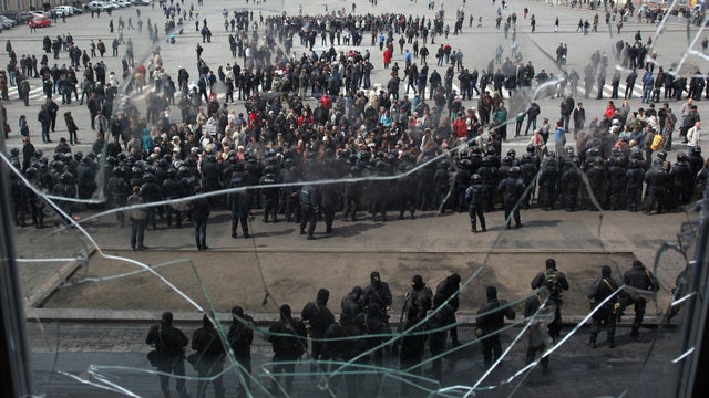 A picture taken through a shattered window shows pro-Russian protesters gathered in front of Ukrainian police officers standing guard in front of the Kharkiv regional state administration building April 8, 2014. 
