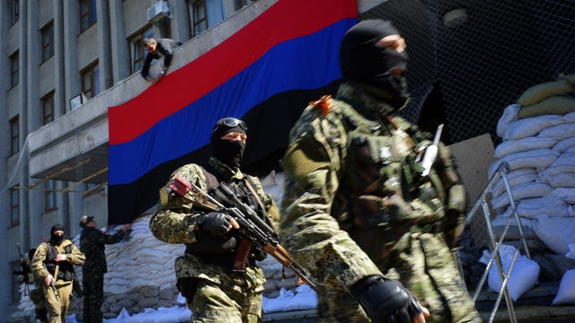 A pro-Russian activist hangs a flag of the so-called "People's Republic of Donetsk" on the regional administration building seized by separatists as armed men in military fatigues guard the premises in the eastern Ukrainian city of Slavyansk 