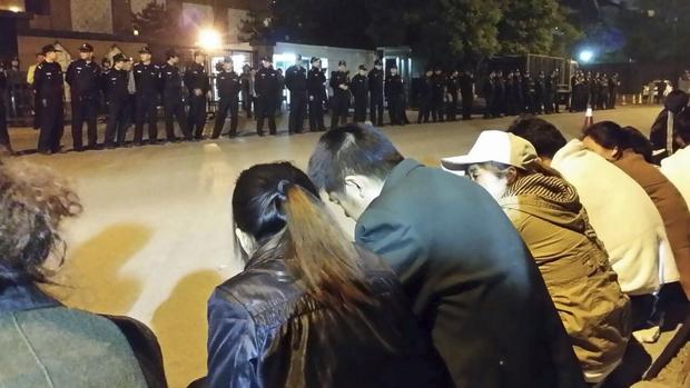 Family members (front) of passengers aboard missing Malaysia Airlines flight MH370 gather for a sit-in protest as security personnel stand guard outside the Malaysian Embassy in Beijing 