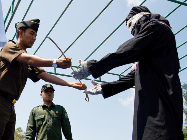A government prosecutor hands over a whip to the executioner before a public caning in Aceh 