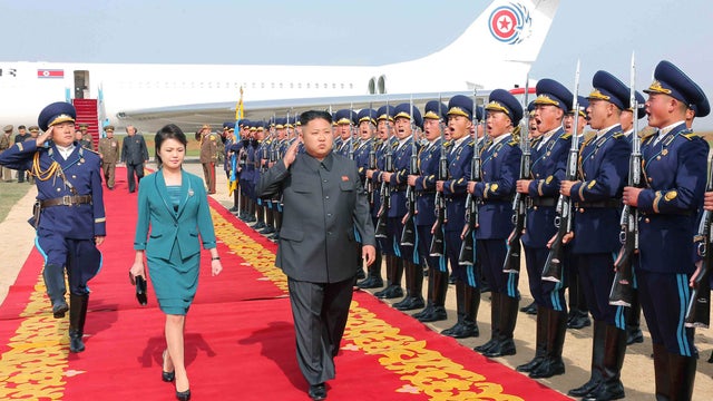 North Korean leader Kim Jong Un salutes as he and his wife Ri Sol Ju walk past an honor guard  